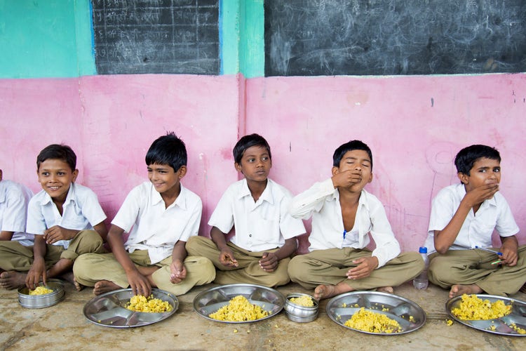 School children sitting on the ground and eating with their hands